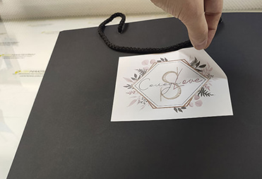 Черный бумажный пакет из дизайнерской бумаги с брендированной наклейкой, печать наклейки на спмоклеящейся бумаге